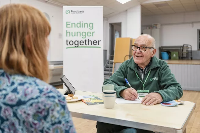 A volunteer speaking to a visitor at a table whilst filling in a form at the Cardiff food bank