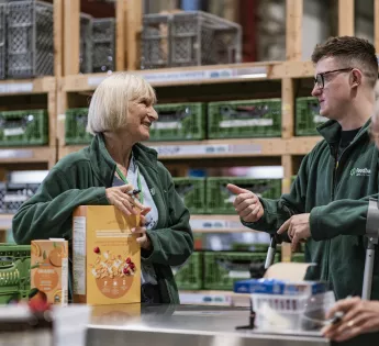 3 people having a chat in front of green crates of donated food
