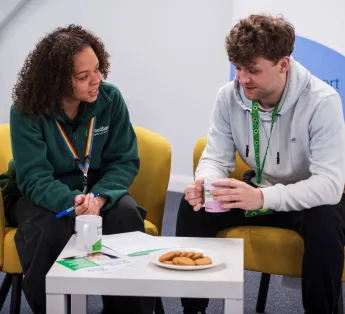 Two people sit and talk with cups of tea and biscuits