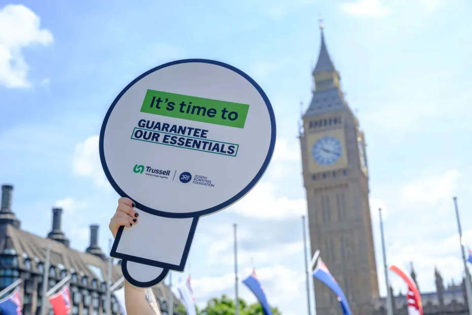 Sign saying "It's time to Guarantee our Essentials" in front of Parliament