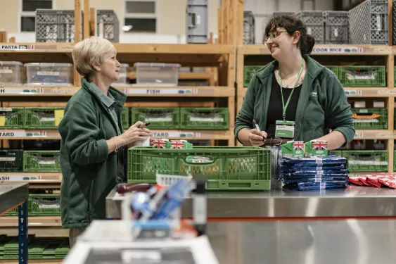 Two women talking whilst packing food containers at Cardiff food bank