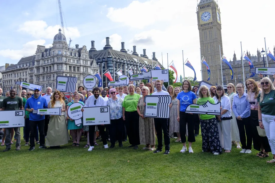 Large group of people holding Guarantee Our Essentials placards with Houses of Parliament in the background