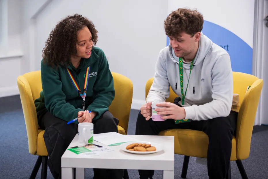 Two people sit and talk with cups of tea and biscuits