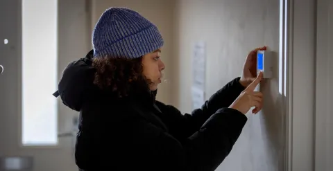 Woman wearing a hat and coat indoors, looking at thermostat