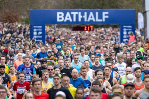 Large crowd of runners coming towards the camera after going through a timing banner